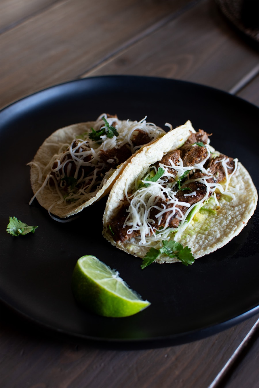 Two crispy tacos with lime on a slate plate
